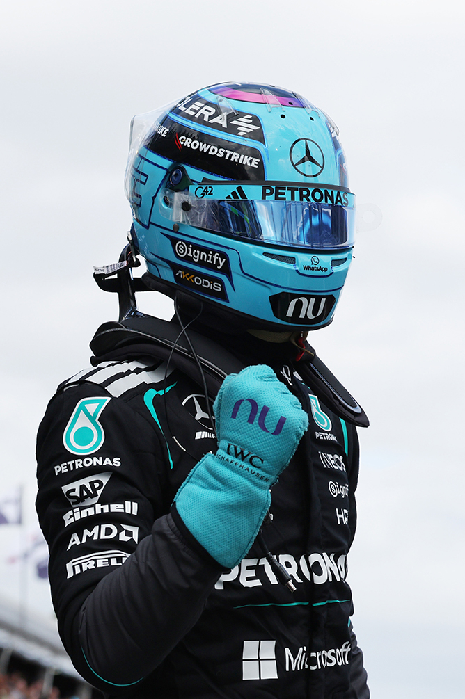 Formula 1 driver wearing a blue helmet and racing suit at the racetrack.